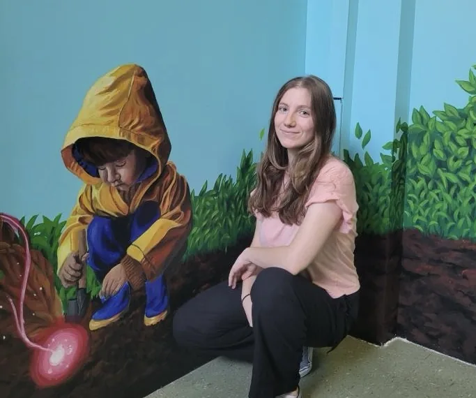 Morgane Cachia devant sa murale : un enfant en imperméable jaune qui creuse la terre