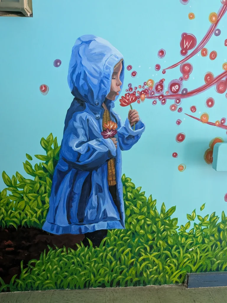 Murale : un enfant en imperméable bleu respire une fleur d’où s’échappent des lettres